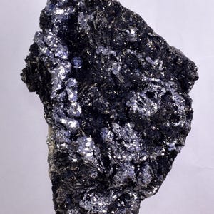 Puede incluir: Una roca grande de color gris oscuro con una superficie rugosa y desigual. La roca está cubierta de pequeños cristales brillantes de color plateado.