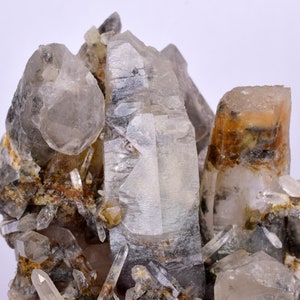 Puede incluir: Un grupo de cristales de cuarzo transparentes con un tono gris ahumado. Los cristales están incrustados en una matriz de roca marrón y gris.