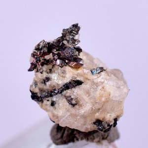 Puede incluir: Un grupo de cristales de plata metálica en una matriz blanca. Los cristales son afilados y tienen un brillo metálico.