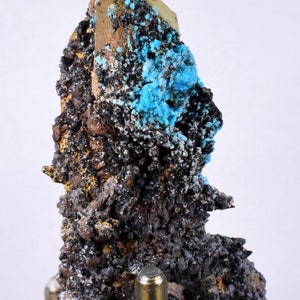 May include: A golden crystal with blue mineral inclusions on a metal stand. The crystal is rough and has a natural, earthy look.