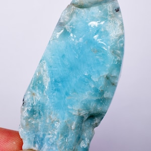 Puede incluir: Un gran cristal de aguamarina azul claro con una textura rugosa y natural. El cristal es translúcido y tiene un aspecto ligeramente nublado.
