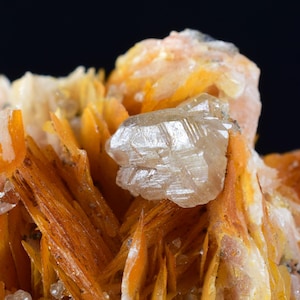 Puede incluir: Primer plano de un grupo de cristales naranja y blancos. Los cristales son afilados y tienen un brillo vítreo.