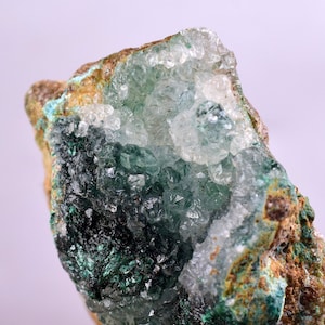 Puede incluir: Un primer plano de una muestra mineral verde y blanca con una superficie rugosa y texturizada. El mineral tiene una estructura cristalina y parece translúcido.