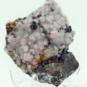 Puede incluir: Un espécimen mineral rosa y blanco con acentos negros y dorados. El espécimen está sobre un fondo gris.