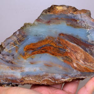 Może przedstawiać: Duża płyta agatu niebieskiego i brązowego z wirującym wzorem. Agat ma gładką, wypolerowaną powierzchnię i jest pięknym przykładem tego typu kamienia szlachetnego.