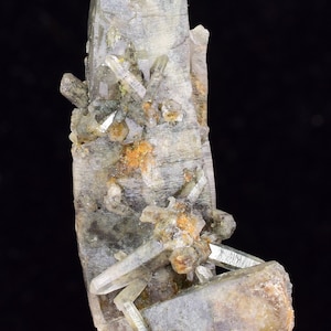 Puede incluir: Un gran cristal de cuarzo transparente con cristales de cuarzo transparentes más pequeños unidos a él. El cristal más grande mide aproximadamente 15 cm de alto y tiene una punta puntiaguda. Los cristales más pequeños están agrupados alrededor de la base del cristal más grande. Los cristales son translúcidos y tienen un ligero tono amarillo.