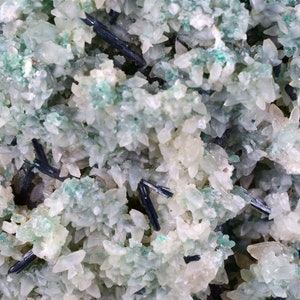 May include: A close-up of a cluster of white and green crystals with black crystals interspersed throughout.