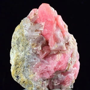Puede incluir: Un vibrante espécimen mineral de rodocrosita rosa con formaciones cristalinas. La rodocrosita es de un color rosa brillante, contrastando con la matriz blanquecina y gris. Se muestra sobre un fondo negro.