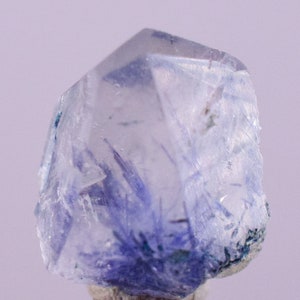 May include: A clear quartz crystal with blue inclusions. The crystal is faceted and has a pointed tip. The inclusions are scattered throughout the crystal and give it a cloudy appearance.