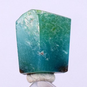 May include: A large, faceted, teal blue and green gemstone with a rough, natural finish. The gemstone is mounted on a white string.