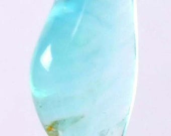 May include: A translucent, teardrop-shaped gemstone in shades of light and deep teal blue. The polished stone has a smooth surface with internal veining and a slight yellow-orange inclusion near the base. The gem is set on a gray surface.
