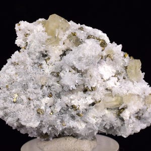 May include: A cluster of white calcite crystals with a few golden pyrite crystals and a large, clear, yellow crystal.