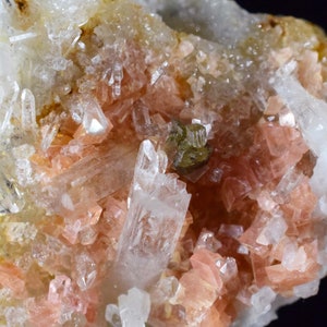 Puede incluir: Un grupo de cristales rosados y blancos en una matriz. Los cristales son translúcidos y tienen un brillo vítreo. La matriz es de color gris oscuro.