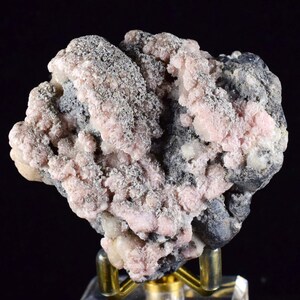 May include: A cluster of pink and grey crystals on a black matrix. The crystals are small and have a rough texture. The matrix is rough and has a dark grey colour.