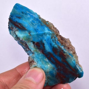 Op de afbeelding: Een ruw, natuurlijk stuk turquoise met een blauwe en groene kleur en rode en bruine aderen. De turquoise is een ruwe, onbewerkte steen.