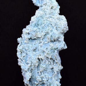 May include: A light blue mineral specimen with a textured, bubbly surface. The mineral has a unique, organic shape and is set against a black background. The color is a soft, pale blue with hints of green.