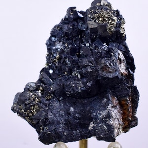 Könnte beinhalten: Ein dunkelgraues Mineralstück mit einem Cluster kleiner, glänzender Kristalle. Das Stück ist auf einem klaren Ständer mit goldener Basis montiert.