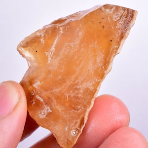 Puede incluir: Un gran cristal natural translúcido de color naranja-marrón, cortado en bruto, con una punta.