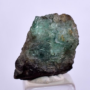 May include: A rough, green emerald crystal with a dark gray matrix. The crystal has a glassy luster and is partially translucent.
