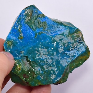 Może przedstawiać: Surowy, nieregularny kawałek niebiesko-zielonego kamienia szlachetnego. Kamień ma marmurkowy wygląd z obszarami głębokiego błękitu i zieleni.