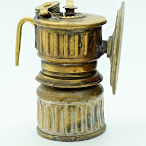May include: A brass miner's lamp with a round reflector and a handle. The lamp has a worn, aged finish.