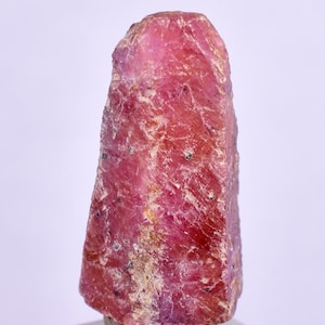 Puede incluir: Un cristal de rubí rojo intenso con una superficie rugosa y natural. El cristal es de un color rojo vibrante y tiene una forma puntiaguda.