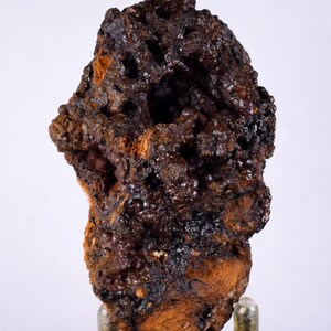 Könnte beinhalten: Ein dunkelbraunes, unregelmäßig geformtes Mineralstück mit einer rauen, porösen Oberfläche. Das Mineral hat einen metallischen Glanz und scheint aus kleinen, kristallinen Strukturen zu bestehen.