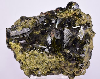 May include: A dark green mineral specimen with sharp, crystal formations. The crystals are a deep, reflective green, contrasting with the lighter, mossy green matrix. The overall structure is jagged and textured.