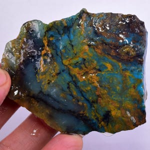 Może przedstawiać: Surowy, naturalny kawałek opalu niebieskiego i żółtego z ciemną, prawie czarną żyłą przechodzącą przez niego. Opal ma gładką, wypolerowaną powierzchnię i jest pięknym przykładem tego kamienia szlachetnego.