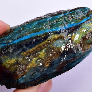 Może przedstawiać: Duży, surowy, niebieski i zielony kamień szlachetny z paskowanym wzorem. Kamień ma gładką, wypolerowaną powierzchnię i jest półprzezroczysty.