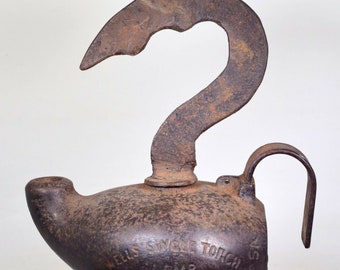 May include: A vintage Wells Single Torch Lamp with a cast iron construction. The lamp has a unique hook-shaped handle and a spout for oil. The lamp is marked "Wells Single Torch Lamp" and "Wells & Co."