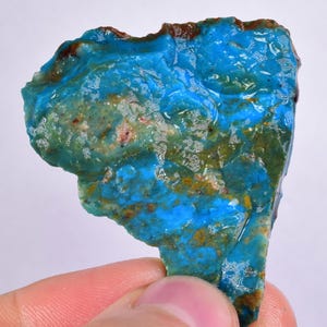 Może przedstawiać: Szorstki, nieregularny kawałek turkusu o żywym niebiesko-zielonym wzorze. Turkus ma naturalne, nieoszlifowane wykończenie i wykazuje różnorodne tekstury.