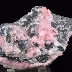 May include: A cluster of pink and grey crystals on a dark background. The crystals are arranged in a random pattern and have a rough, textured surface.