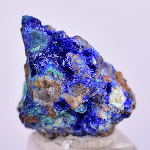 May include: A cluster of blue azurite crystals with a few clear quartz crystals embedded in the matrix. The azurite crystals are a deep blue color and have a rough, textured surface.