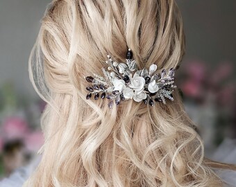 May include: A silver hair comb with white and purple flowers and rhinestones. The comb is in a woman's blonde hair.