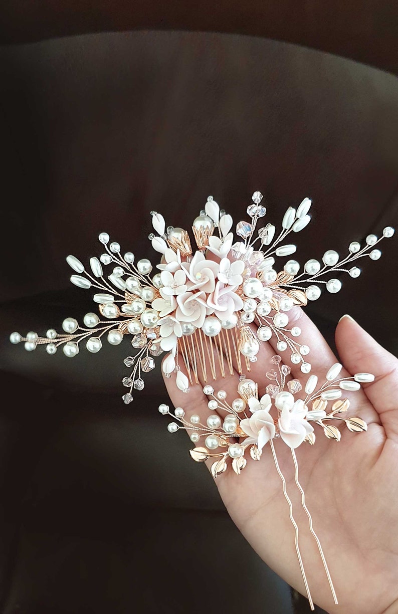 May include: A set of two gold hair combs with white pearl and pink flower accents. The larger comb has a comb base and the smaller comb has two bobby pins.