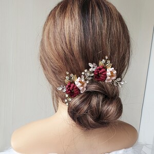 May include: Two burgundy and blush floral hair clips with gold and crystal embellishments. The clips are worn in a woman's hair.