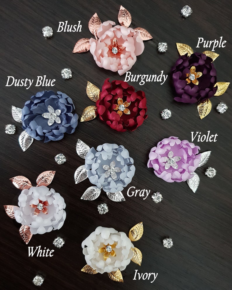 May include: Assortment of ten fabric flower hair clips in various colors, including blush, burgundy, dusty blue, gray, ivory, purple, violet, and white. Each flower has a rhinestone center and gold or silver leaf accents.