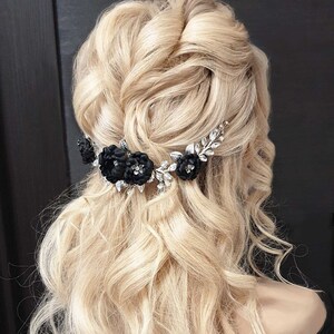 May include: A silver hair comb with black fabric flowers and rhinestones. The comb is worn in a woman's blonde hair.