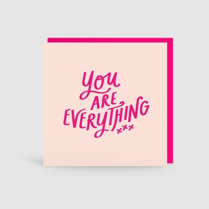 May include: A square greeting card with a light pink front featuring the dark pink text "YOU ARE EVERYTHING xxx" in a handwritten script font. The card is layered over a bright hot pink backing, creating a visible border around the edges.