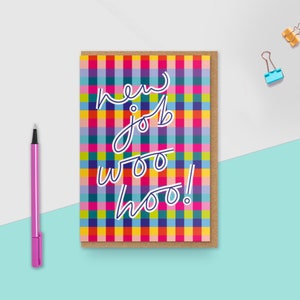 May include: A rectangular greeting card featuring a vibrant, multi-coloured plaid pattern in shades of pink, yellow, blue, and green. The text "new job woo hoo!" is written in a white, cursive-style font across the centre of the card.