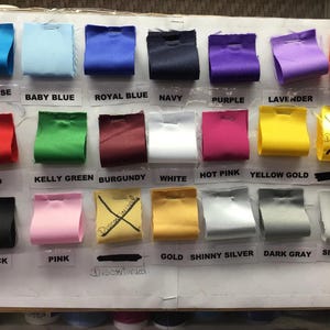 May include: A color chart with 18 different fabric swatches. The swatches are labeled with the following colors: turquoise, baby blue, royal blue, navy, purple, lavender, orange, red, kelly green, burgundy, white, hot pink, yellow gold, black, pink, gold, shiny silver, dark gray, and silver gray.