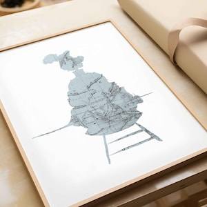 May include: A framed print featuring a light blue map design shaped like a chair. The map has intricate details and is set against a white background. The frame is made of light-colored wood.