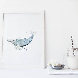 May include: A watercolor painting of a blue whale in a white frame. The whale is swimming to the right and has a light blue body with darker blue accents. The painting is on a white background.