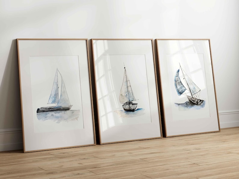 May include: Three framed watercolor paintings of sailboats on a white background. Each painting features a different sailboat with blue and white sails.
