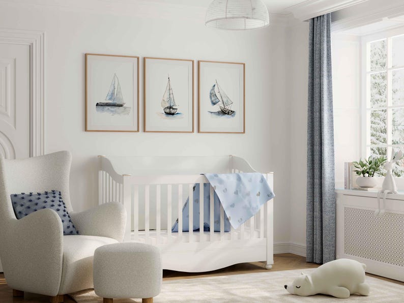 May include: A white crib with a blue and white patterned blanket. A white armchair with a blue and white patterned pillow sits next to the crib. Three framed watercolor paintings of sailboats hang on the wall behind the crib.
