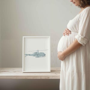 May include: A framed print with a blue helicopter illustration on a white background. The artwork is in a white frame, placed on a wooden surface. The image is set against a neutral backdrop.