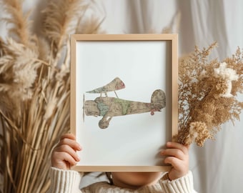 May include: A child holds a framed print of a vintage airplane silhouette made from a world map. The print is in a light wood frame and has a white background.