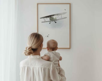 May include: A framed wall art print featuring a light green biplane illustration centered on a white background with soft blue cloud accents and small dark ink splatters, enclosed in a simple light-toned wooden frame.