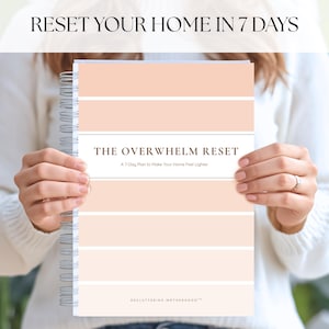 May include: A spiral-bound planner with a peach and white striped cover is held by a person. The title "THE OVERWHELM RESET" is displayed, with the subtitle "A 7-Day Plan to Make Your Home Feel Lighter." The text "RESET YOUR HOME IN 7 DAYS" is at the top.